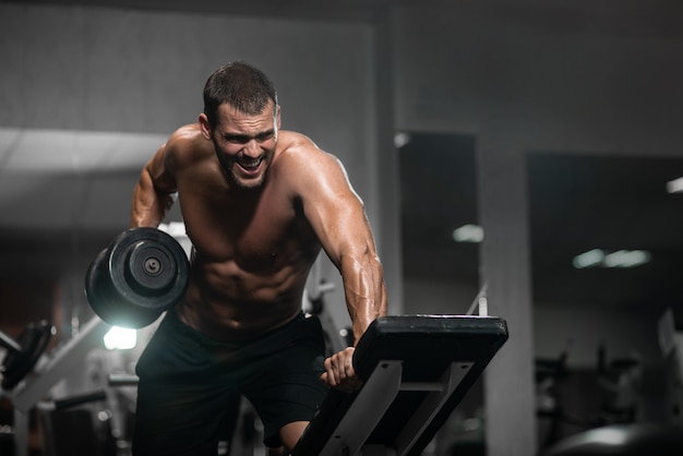 Photo athletic man trains with dumbbells, pumping his biceps