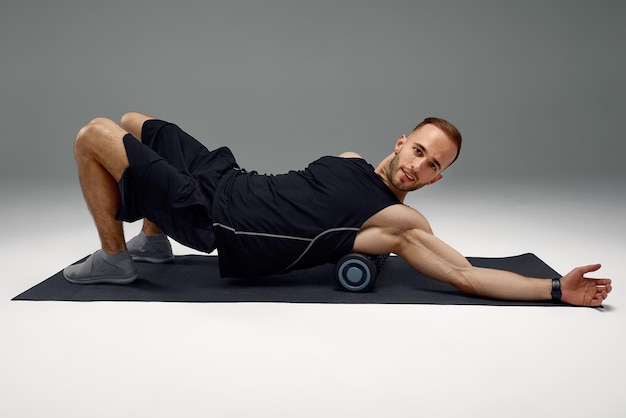 Uomo atletico che utilizza un rullo di schiuma per alleviare i muscoli doloranti dopo un allenamento
