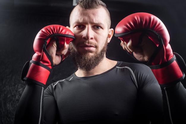 An athletic man wearing red kickboxing gloves posing and ready to fight in the gym