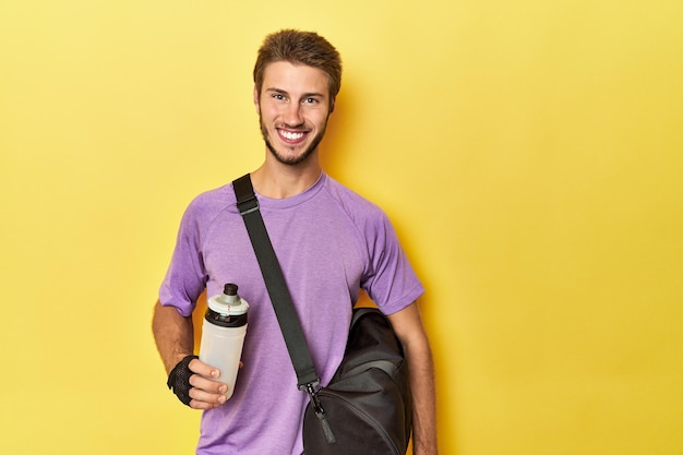 Athletic man with backpack gloves and water bottle on yellow studio backdrop