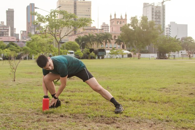 Athletic man with headphones stretching in the park with the city in the background.