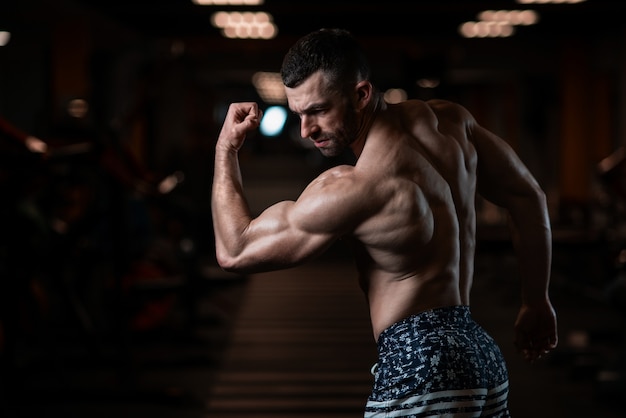 Uomo atletico con un corpo muscoloso pone in palestra, mostrando il suo bicipite. il concetto di uno stile di vita sano