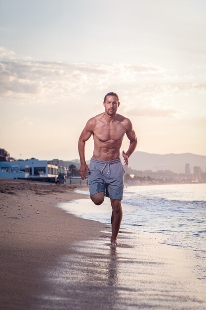 Спортивный (ый) человек, тренирующийся на пляже на рассвете