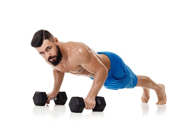 Athletic muscular man doing exercises push up with dumbbells. Strong bodybuilder with naked torso on white background