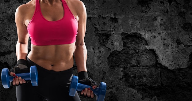 Athletic muscular woman training biceps with dumbbells on grunge background