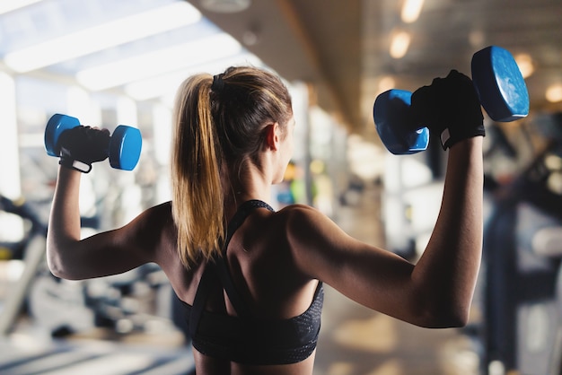 Foto donna muscolare atletica allena bicipiti con manubri in palestra