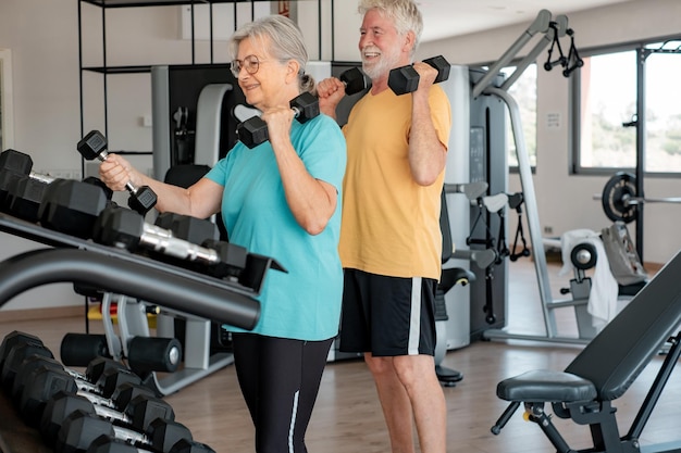 Photo athletic senior couple keeping fit working out together in the gym doing dumbbell lifting exercise