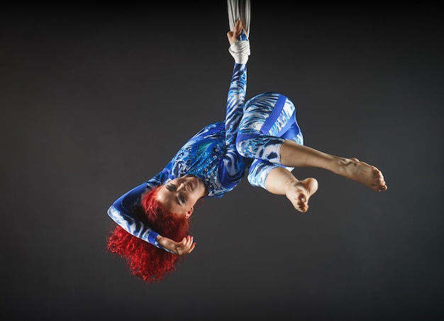 Foto artista di circo aerea sexy atletico con rossa in costume blu che balla nell'aria con equilibrio.