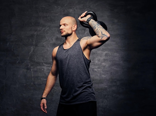 Athletic shaved head tattooed male doing shoulder workout with the Kettlebell.