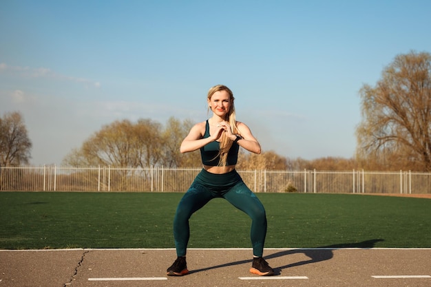 写真 春に野外運動をしているスタジアムでスクワットをしているアスレチックスリムな女性