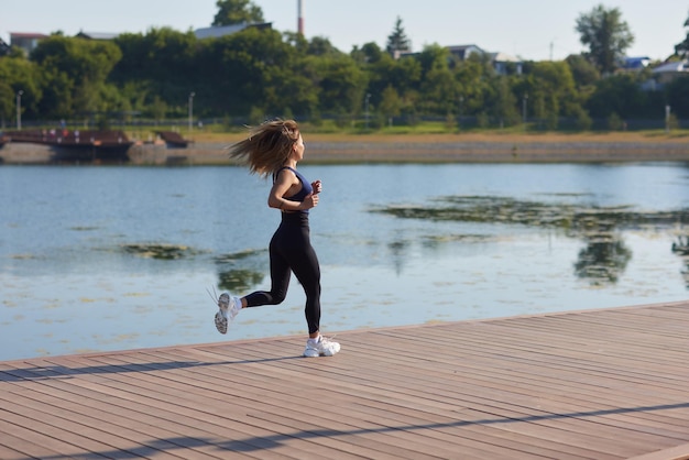 La donna snella atletica in una giornata di sole corre lungo l'argine o il parco