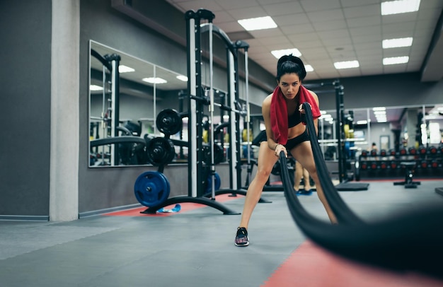 Athletic sportive young fit female working out in functional training gym doing crossfit exercise with battle ropes copyspace for your text Crossfit workout motivation People sport concept