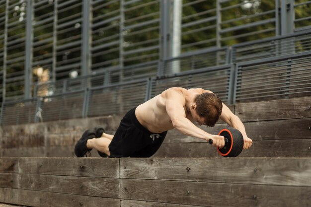 Athletic sporty caucasian shirtless man doing exercise with abs roller wheel