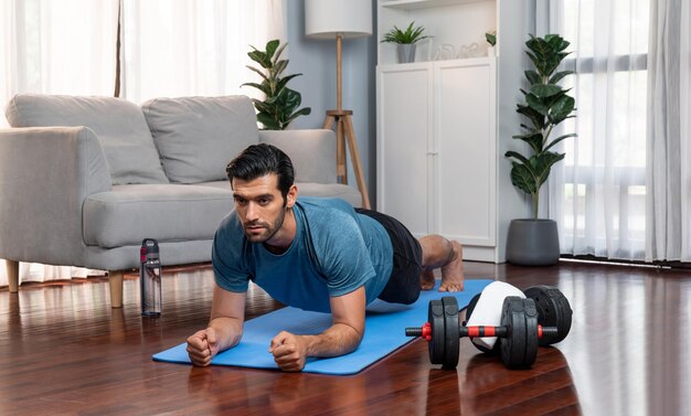 Athletic and sporty man doing plank on fitness mat at gaiety home