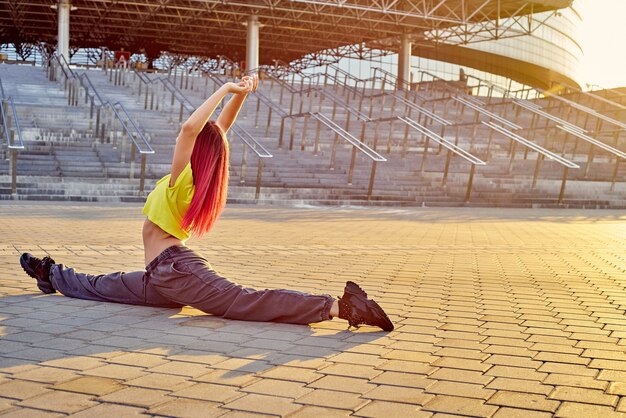 Athletic sporty woman with dyed pink hair sat on splits before training of sunset