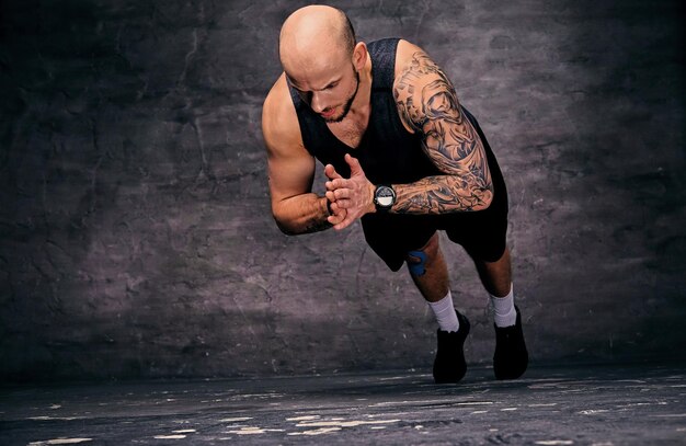Спортивный татуированный мужчина с бритой головой делает отжимания с прыжками.