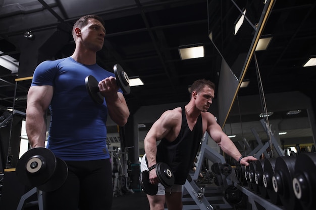 Photo athletic twin brothers bodybuilders training together at the gym doing dumbbells exercise