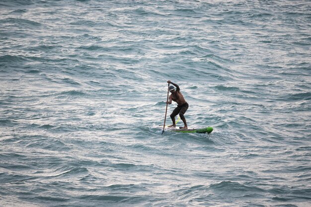 athletic wiry surfer guy swims with a paddle on a sup board in the sea Stand up paddleboarding