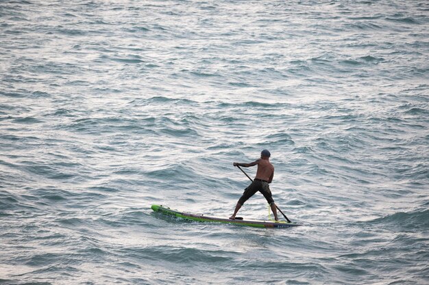 Спортивный серфер плывет с веслом на доске в море Stand up paddleboarding