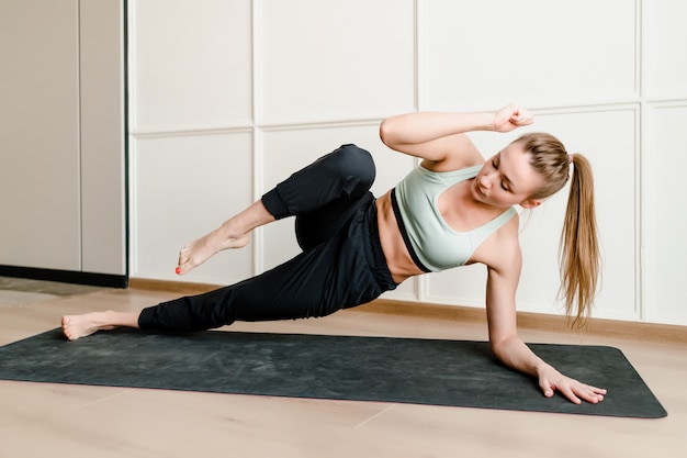 Athletic woman doing physical exercise at home on yoga mat