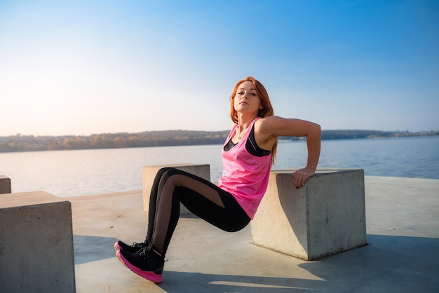 Athletic  woman doing squatting exercise in sunny park near the lake.   Concept of wellness and healthy lifestyle