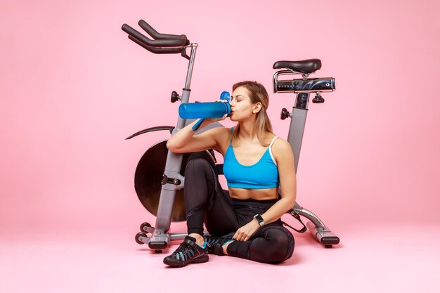 Athletic woman drinking water from bottle restoring water balance after exhausted workout