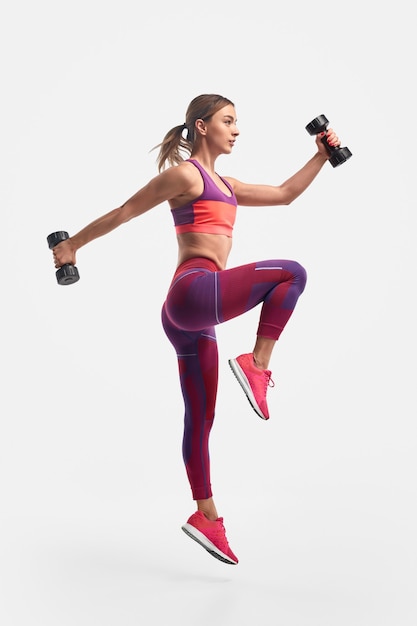 Photo athletic woman jumping with dumbbells