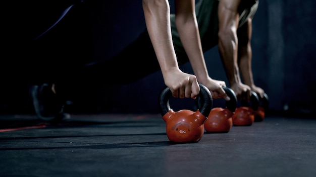 Athletic woman and man with kettlebell dumbbell during cross training at fitness gym. Health and muscles flexing.