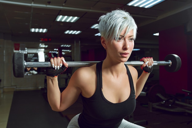 Athletic woman pumping up muscles with barbell in the fitness room