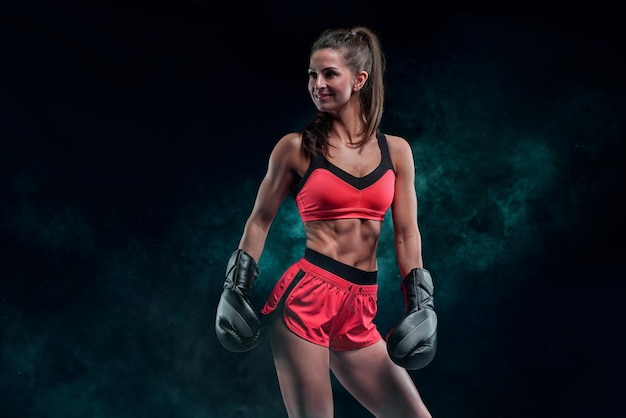 Athletic woman in red shorts and top posing against a dark smoky background Boxing and mixed martial arts concept