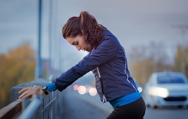 Athletic woman resting after jogging and leaning on a parapet of the bridge