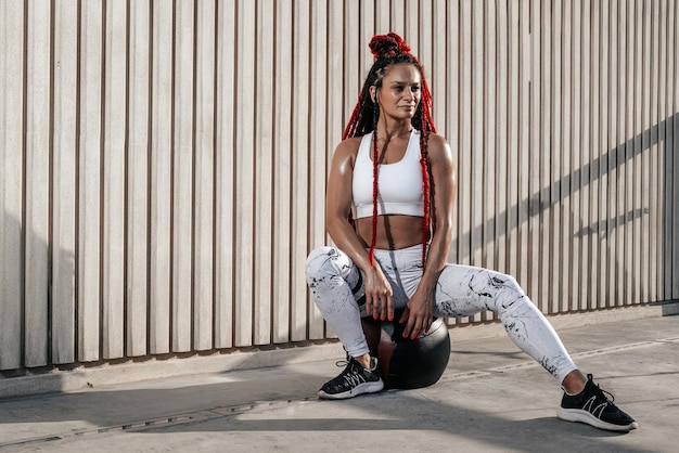 Athletic woman sitting with his leg outstretched with med ball Strength and motivationPhoto of sporty woman in fashionable sportswear