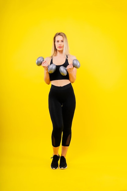 Athletic woman in sportswear raises dumbbells leads healthy lifestyle has happy expression