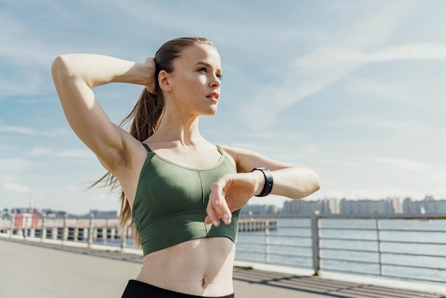 Athletic woman stretching her arm wearing a fitness tracker with a serene waterfront backdrop