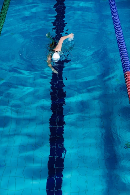 Спортивная (ый) женщина, плавающая в плавательной шляпе и очках в бассейне