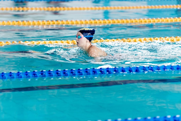 スイミングプールで水泳帽とメガネで泳ぐ運動女性