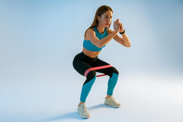 athletic woman trains legs with fitness elastic band on studio background