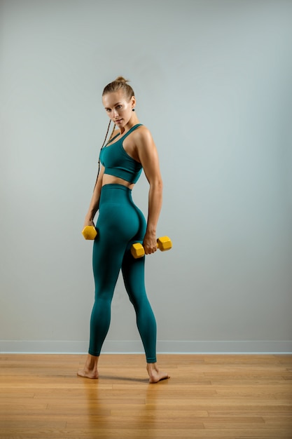 Athletic woman with dumbbells in hands on a gray