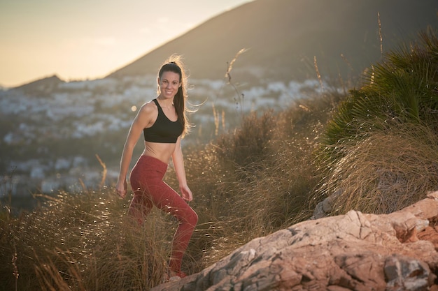 спортивная женщина с длинными волосами и красными леггинсами поднимается в гору в горах