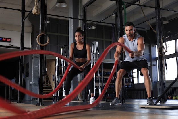 Athletic young couple with battle rope doing exercise in functional training fitness gym.