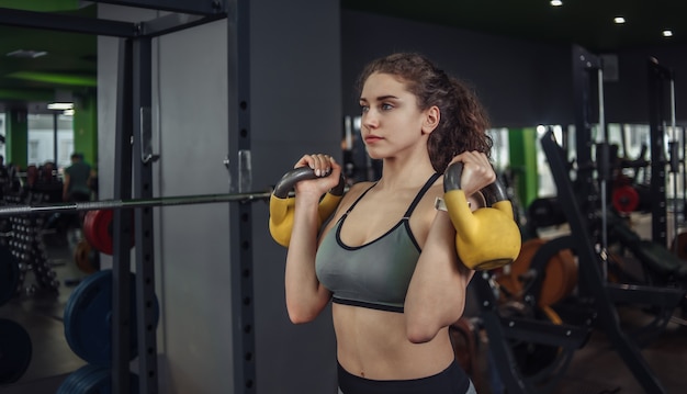 Giovane atletica donna adatta facendo esercizio con kettlebell in palestra. pesi liberi, allenamento funzionale