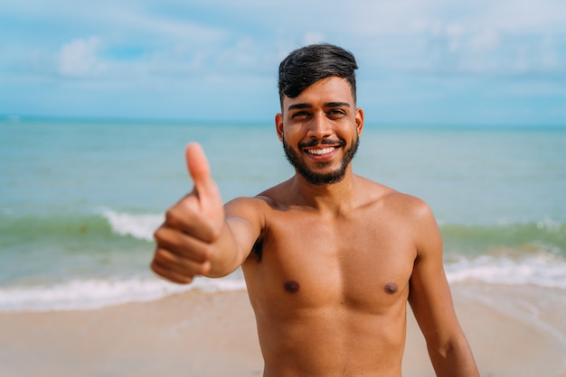 Athletic young latin american man on the beach with thumb up