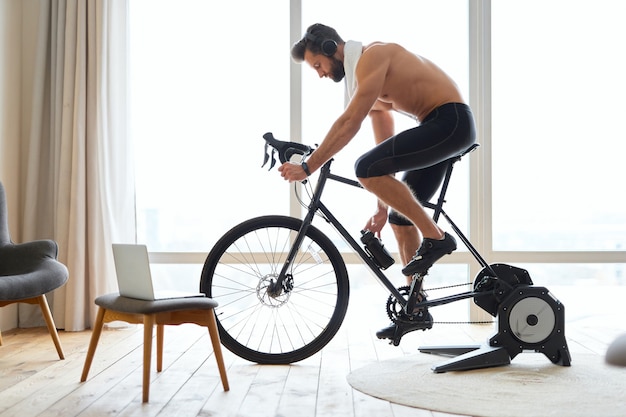 Photo athletic young man listening to music and riding stationery bike