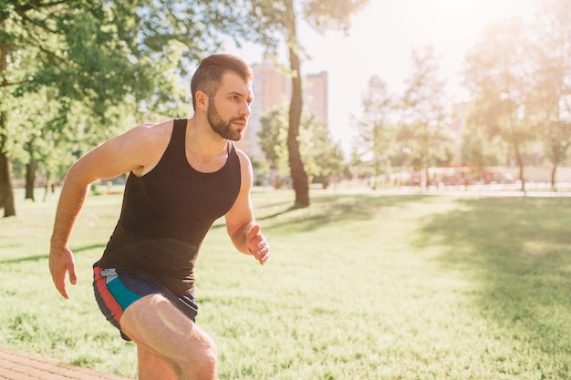 自然の中で走っている運動の若い男。健康的な生活様式。ひげを生やした黒い髪のスポーツマンが道路で実行されている-日没のバックライト