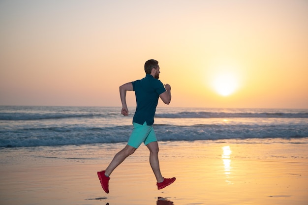 Athletic young man running on sea colorful sunset sky