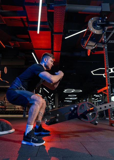 Athletic young man training his body Man doing exercise in modern dark gym