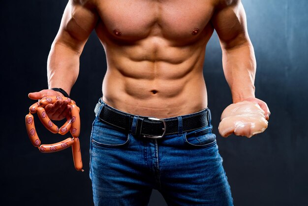 닭 가슴살과 소시지를 들고 운동하는 젊은 스포츠맨 다이어트 및 스포츠 영양 알몸 몸통 근육질의 남자 자른 사진