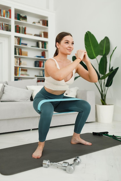 Athletic young woman doing morning exercises squatting alone in the living room serious girl