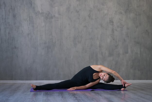 Foto giovane donna atletica che fa yoga isolata su sfondo grigio muro in nero