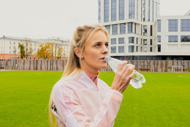 An athletic young woman drinks water during a workout at an outdoor stadium A model in a tracksuit